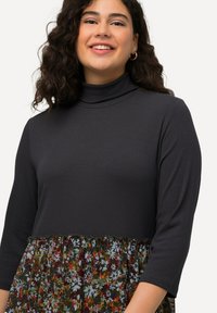 Czarna bluzka z długim rękawem i golfem, wykonana z ciemnoszarego prążkowanego materiału, połączona z dolną częścią w kształcie dzwonu w intensywne, kwiatowe wzory.