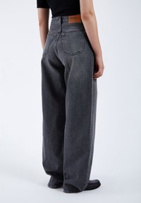 Hochtaillierte Bootcut-Jeans aus dunkelgrauem Denim mit einem Lederetikett am hinteren Bund und zwei Gesäßtaschen. Glatte Textur.