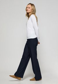 Maglietta bianca a maniche lunghe con scollatura a girocollo, abbinata a pantaloni larghi color navy. L'outfit è completato da scarpe piatte color cammello.