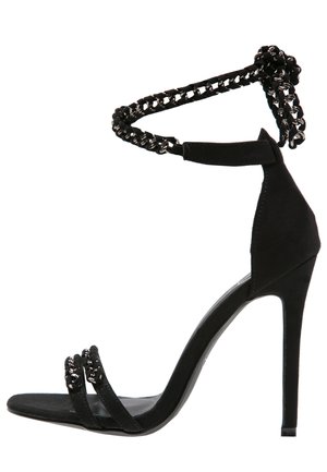 Sandale noire à talons hauts avec une semelle fine, deux brides frontales et une bride de cheville en chaîne tressée noire et argentée.