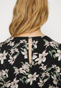 Blommig klänning med svart bakgrund och ljusrosa samt gröna blommönster, rund halsringning, och ett litet nyckelhål i ryggen med knappstängning.