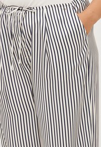 Gestreifte Stoffhosen in Marineblau und Weiß werden gezeigt, mit einem Kordelzugbund und Taschen, die ihr lässiges, stilvolles Design betonen.