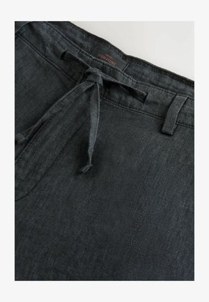 Pantalons en lin noirs avec fermeture à cordon, présentant une texture lisse et un éclat subtile. Comprend des passants de ceinture et une étiquette indiquant "SIGNATURE."