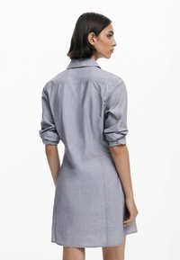 Abito grigio a camicia con colletto, maniche arrotolate e silhouette dritta, con una sottile trama e lunghezza a metà coscia.