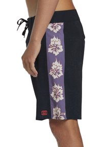 Bañador negro con panel lateral morado que presenta flores de hibisco beige, cinturilla elástica y cordón. Detalle de tejido texturizado visible.