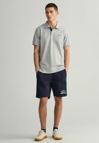 Grå polo skjorte med marineblå krage, parret med marineblå shorts med grønne accenter og hvid tekst. Sko i en lys skygge med tekstureret sål.