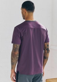 Korte mouw sportshirt van donkerpaars stof met een gestructureerde afwerking, voorzien van een grijze kraag en zijsplitten voor verbeterde bewegingsvrijheid.