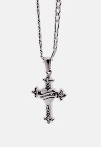 Strieborný prívesok v tvare kríža s detailnými vzormi a srdcom v strede, obklopený stuhou s nápisom "LOS ANGELES" na retiazke.