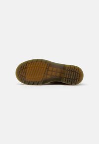 Suola di una scarpa marrone con grip in gomma traslucida e battistrada decorato visibile su uno sfondo bianco.