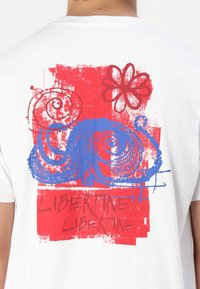 White cotton t-shirt featuring a multicolored graphic design with swirls, a flower, and the text "LIBERTINE LIBERTINE" in red.