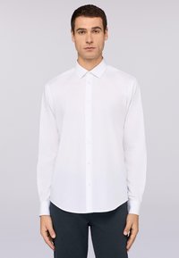 Witte langlopende, knopsluiting overhemd met een klassieke kraag, gladde textuur en ronde zoom, gecombineerd met donkergekleurde broek.