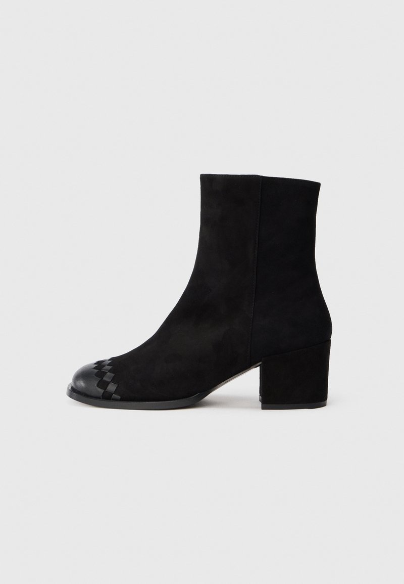 Bottine en daim noir avec talon bloc et détail en cuir tressé sur le bout, vue de profil sur fond uni.