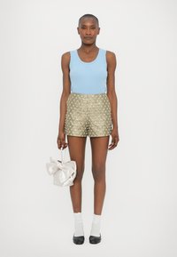 Top bleumarin deschis cu nervuri, pantaloni scurți aurii cu model floral, șosete albe până la gleznă, balerini negri, ținând o geantă roz pal cu o fundă.