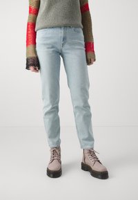 Ljusblå denimjeans med något avsmalnande ben, kombinerade med beige snörda ankelskor med en svart kraftig sula. Tröjan har färgglada randiga ärmar.