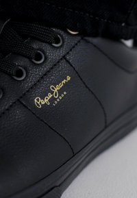 Sapatilhas pretas de couro com superfície texturizada, apresentando atacadores pretos, costura tonal e um logotipo dourado "Pepe Jeans London" na lateral.