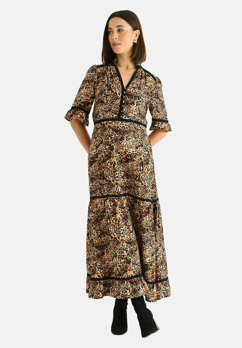 Leopard print maxi dress with black trim. Features a V-neckline, puff sleeves, and tiered skirt. Styled with black ankle boots.