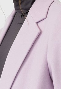 Lavendel ullblandad kavaj med spetshalskrage, strukturerad yta och definierad silhuett, lagd över en mörkgrå polotröja.