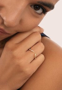 Guldringar med släta kurvor och flerfärgade stenar. Ringarna ligger på en hand med naturlig hudton, vilket visar fina detaljer och accenter.