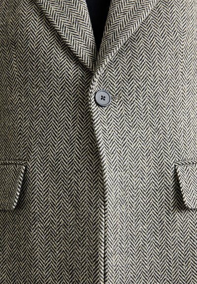 Herringbone-patterned blazer in gray and cream, featuring a notched collar, single button closure, and side pockets with contrasting stitching.