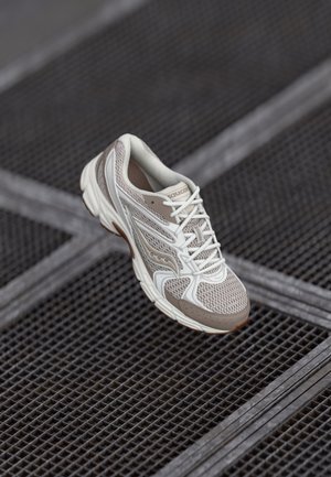 Lekki but do biegania w beżowej i białej siateczce, z amortyzowaną podeszwą, skomplikowanymi liniami wzoru i zapięciem na sznurówki.