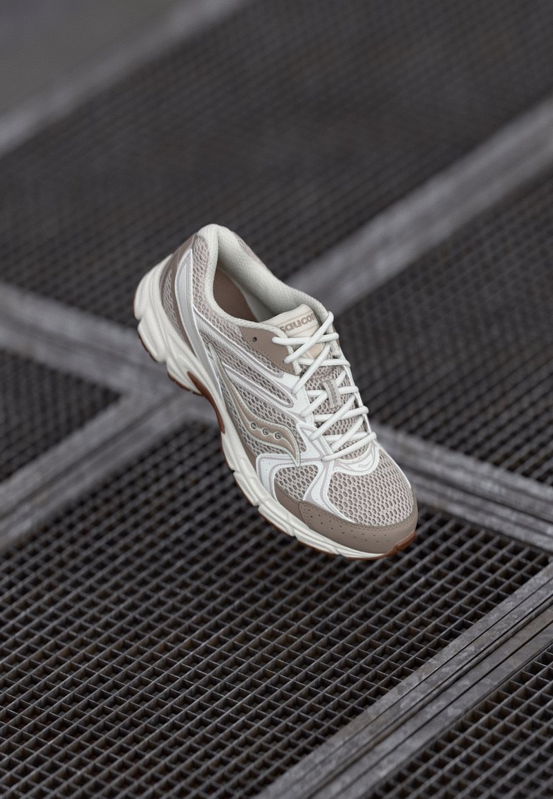 Lightweight running shoe in beige and white mesh, featuring a cushioned sole, intricate design lines, and lace-up closure.