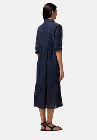 Abito blu navy con orlo a strati, realizzato in tessuto perforato. Presenta maniche corte, colletto con bottoni e un dettaglio di vita arricciata.