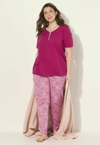 Fuchsia T-shirt met korte mouwen, een V-hals en knoopaccenten, gecombineerd met roze paisley-gepatenteerde broeken. Zacht, licht materiaal met een relaxte pasvorm.