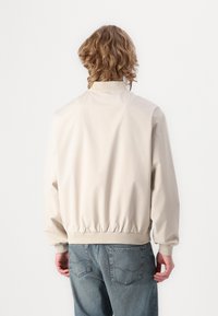 Beige bomberjakke med elastiske manchetter og kant, lavet af glat stof; har en klassisk krave og en afslappet pasform.