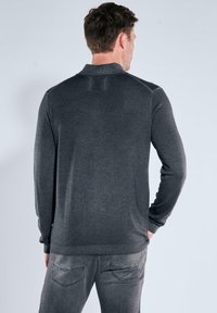 Graues Langarm-Polohemd mit geripptem Kragen und subtiler Textur, von hinten gezeigt. Kombiniert mit grauen Jeans mit Taschenverzierungen.