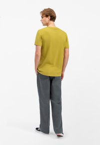T-shirt verde oliva a maniche corte con scollo rotondo, abbinato a pantaloni grigi larghi e sneakers nere. Tessuto semplice e morbido.