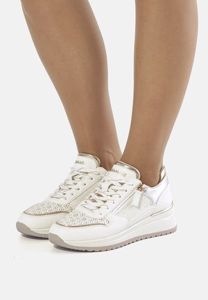 Zapatillas blancas con detalles dorados, diseño perforado, cordones y cremallera lateral. La suela es texturizada con una ligera forma de cuña.