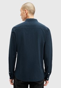 Námořnická košile s dlouhým rukávem vyrobená z texturované látky, s límcem na knoflíky, bočními rozparky a knoflíkovými manžetami, se zaobleným lemem.