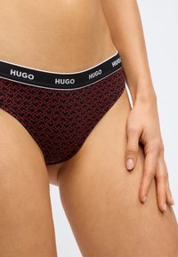 Εσώρουχα Hugo σε κόκκινο και μαύρο με σχέδιο καρδιές και μαύρη μέση με το λογότυπο. Λείο ύφασμα με εφαρμοστή σχεδίαση.