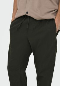 Pantalones casuales negros con cinturilla ajustable, que cuentan con bolsillos laterales y un corte ligeramente holgado, hechos de una tela suave y texturizada.