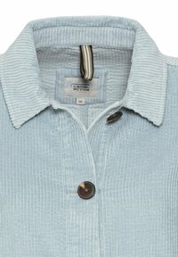 Lichtblauwe corduroyjack met knoopsluiting, een omklapbare kraag en een geweven label. De stof heeft een verticale ribbeltextuur.