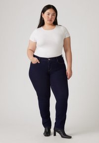 Vit kortärmad topp kombinerad med mörkblå, figurnära jeans. Jeansens har standardfickor och en diskret söm. Svarta stövlar med klack kompletterar outfiten.