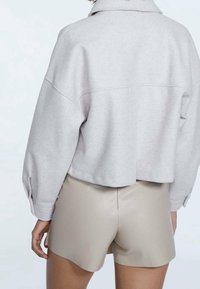 Przycięta, jasnoszara bluza z kołnierzem do założenia na zakładkę i opuszczanymi ramionami, w połączeniu z beżowymi, gładkimi szortami.