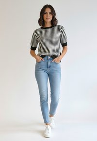 Czarnobiały dzianinowy top w kratę z krótkimi rękawami, zestawiony z jasnoniebieskimi obcisłymi jeansami z wysokim stanem i białymi trampkami.