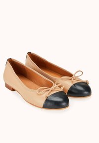 Ballet flats en cuir nude avec un capuchon en cuir noir, talon plat et détail en nœud à l'avant. Surface lisse avec une texture légère.