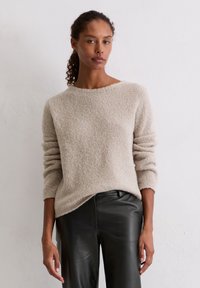 Jasno beżowy, teksturowany sweter z okrągłym dekoltem i długimi rękawami, w zestawieniu z czarnymi skórzanymi spodniami. Prosty i nowoczesny design.