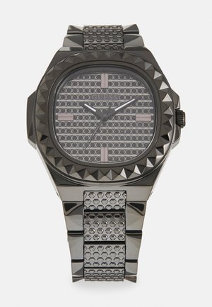 Sort rustfrit stål ur med et oktagonal urkasse, spidse bezel, tekstureret sølvfarvet skive og rem med hexagonal mønster.