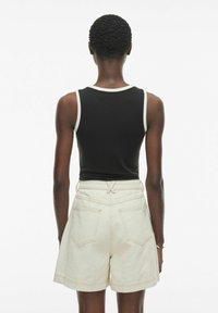 Zwarte aansluitende tanktop met contrasterende witte rand, gecombineerd met lichtbeige hoge taille shorts met twee achterzakken en zichtbare stiksels.