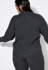 Suéter de punto gris oscuro con un corte relajado, dobladillo acanalado y hombros caídos. Textura suave, mangas largas y un diseño sencillo.