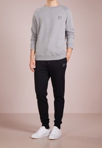 Sudadera de felpa gris con cuello redondo y puños de canalé, combinada con pantalones jogger negros con un parche de acento, complementada con zapatillas blancas.