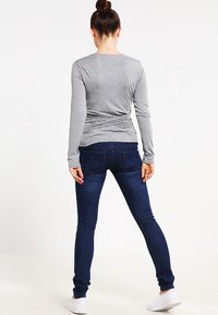 Gray long-sleeve top with back twist detail paired with dark blue skinny jeans, featuring pockets and a tapered fit, worn with white sneakers.