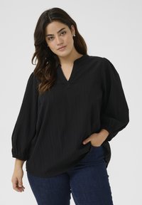 Schwarze Bluse mit V-Ausschnitt und Ballonärmeln, die über senkrechte Streifen und eine lockere Passform verfügt. Das Material wirkt leicht und texturiert.