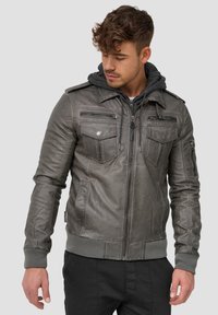 Chaqueta de cuero gris con capucha, con bolsillos en el pecho con cremallera y bolsillos laterales, puños y dobladillo acanalados, y hombreras de estilo militar.