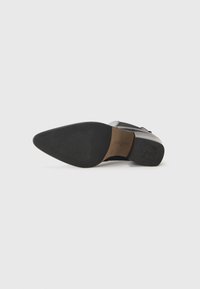 Semelle de chaussure en cuir noir avec un design à bout pointu. Comprend une étiquette contrastante en tan et une surface texturée pour une meilleure adhérence et stabilité.