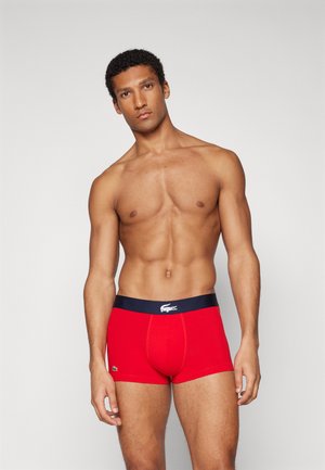 Boxer shorts rojos con una cintura azul marino que presenta un logo. Fabricados con una tela suave, tienen un diseño ajustado y piernas cortas.