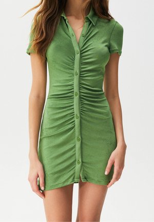 Mujer con un vestido de manga corta color verde claro con botones y detalles fruncidos en el centro delantero.